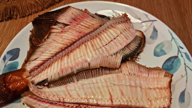 Close-up of a cooked and filleted flatfish with its spine and bones visible, prepared for a delicious meal on a decorative plate - push in