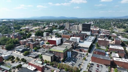 Downtown Lynchburg, Virginia, with historic architecture, modern buildings, surrounded by green hills and framed by distant Blue Ridge Mountains in vibrant cityscape. Aerial wide shot. - Powered by Adobe