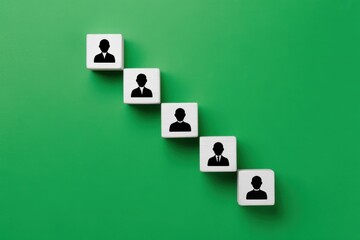 Top-down view of wooden blocks with business person icons arranged in a descending line, symbolizing corporate hierarchy, organizational structure, and team management on a green background