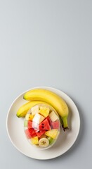 Fresh fruit salad in plastic container with bananas on plate.
