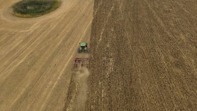 Aerial view of a vibrant green tractor tilling the golden field creating a stark contrast between the tilled and untilled land, Bedford, England, United Kingdom.