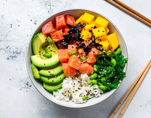 Top view of a fresh poke bowl with diced salmon, avocado slices, mango, rice, seaweed salad and edamame beans, sprinkled with sesame seeds. Healthy Hawaiian-Japanese fusion food concept.