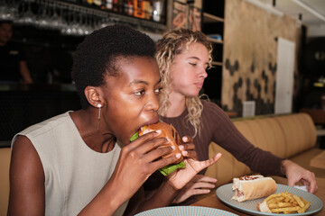 Woman eating hamburger with friend at restaurant