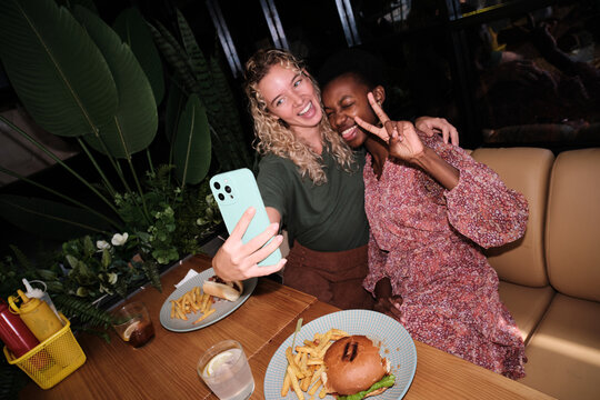 Diverse women friends taking selfie at restaurant - Powered by Adobe
