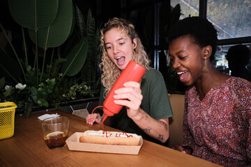 Diverse friends laughing adding ketchup to hot dog