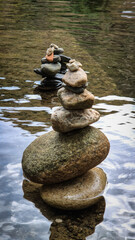 Stacks of balanced river pebbles on the water’s edge symbolize harmony, peace, and focus. Reflective surface and smooth stones evoke zen, mindfulness, and natural art.