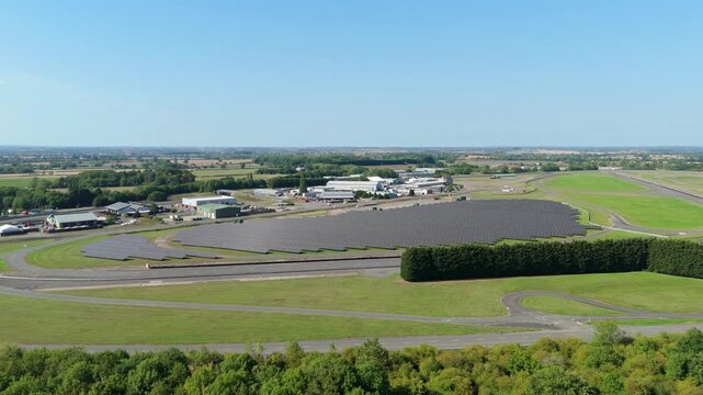 Aerial view of expansive solar panels and buildings blending with the green landscape under a clear sky, Nuneaton, England, United Kingdom.