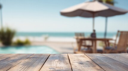 A serene beach view with a wooden table in the foreground and soft-focus patio furniture and an umbrella in the background.