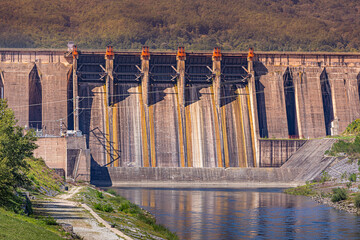 Concrete dam wall with multiple spillways holding back river water, using sustainable energy for...