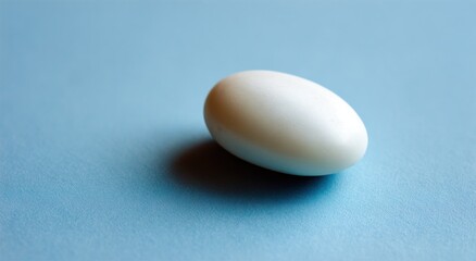 A smooth, oval-shaped white object rests on a textured light-blue surface, casting a subtle shadow.