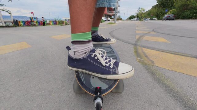 Close-up of feet in sneakers riding a surfskate on a seaside promenade, low angle view with ocean and stormy sky in background
