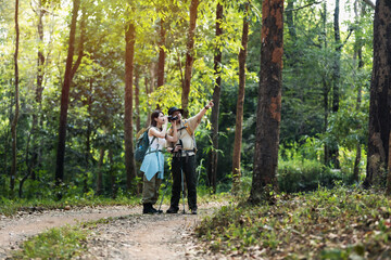 Fototapeta premium Young Asian couple hiking trough forest and watching birds on summer vacation.