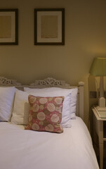 English double bed with white pillows and floral cushions beneath two framed prints, concept of traditional bedroom, quiet rest and interior styling in a countryside home