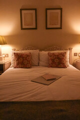 Cosy English bedroom at night with lit lamp, carved headboard, floral cushions and closed laptop with notebook on bed, concept of evening routine, home comfort and quiet retreat