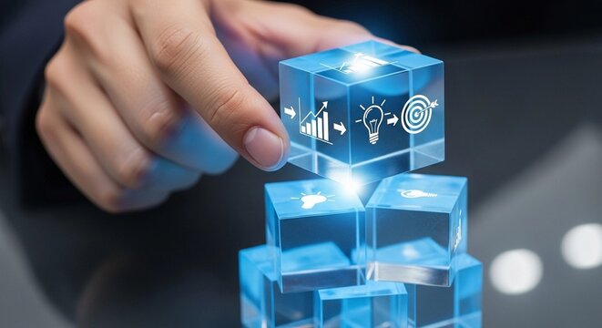 A hand places a glowing blue cube with business icons onto a stack of transparent blocks, symbolizing strategic development and innovation.