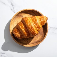 Golden croissant on wooden plate, marble background
