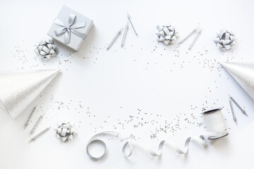 Frame of festive party decoration with silver streamers and gift box and carnaval caps on white background, top view