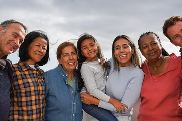 Group of multi generational people hugging each other while smiling on camera - Multiracial friends having fun together outdoor