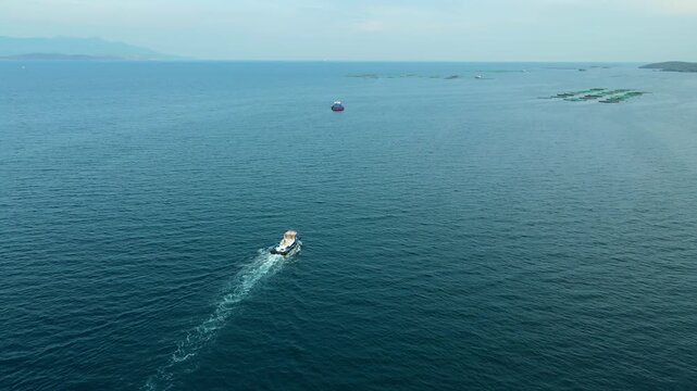 Workboat crossing between aquaculture fish farm sites over open water, aerial. Routine maintenance on aquaculture cage structures