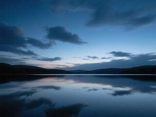 Obraz premium Serene twilight over a calm lake reflecting the dramatic moody sky with clouds painting the horizon in cool blue tones