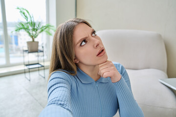 Selfie portrait happy beautiful thinking young woman in home interior