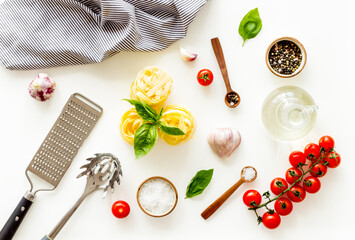 Fettuccine with ingredients for cooking pasta - tomatoes and basil with garlic - on a white background, top view. Flat lay