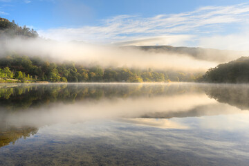 Beautiful autumn morning reflections at Rydal Water with golden light and mist in The Lake District, UK.