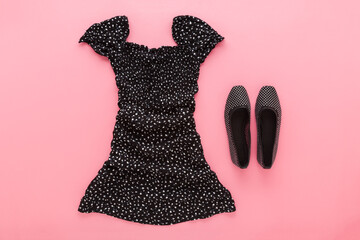 Dark black new casual summer dress and shoes on light pink table background. Pastel color. Closeup. Female accessories. Top down view.