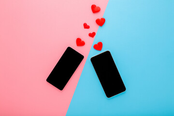 Smartphones with dark black touch screen and red heart shapes on light pink blue table background. Pastel color. Two sides. Love concept. Online dating. Closeup. Flat lay. Top down view.