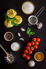 Fettuccine with ingredients for cooking pasta - tomatoes and basil with garlic - on a black background, top view. Flat lay