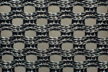 Macro closeup of black synthetic woven fabric mesh with braided threads and geometric grid pattern