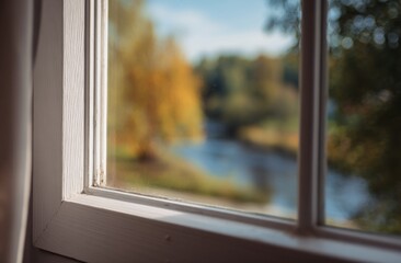 Fototapeta premium Window view of a serene autumn landscape with a river and colorful trees.