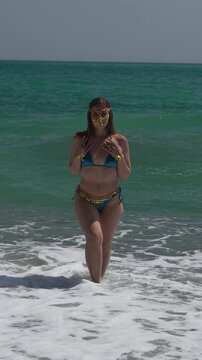 Woman beach ocean, mysterious beautiful woman in exotic golden mask bikini on turquoise beach. Vertical video.