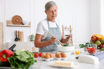 Senior woman cooking salad at white marble table in kitchen