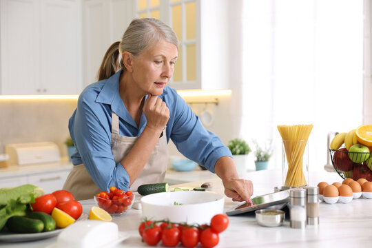 Senior woman using tablet while cooking at white marble table in kitchen - Powered by Adobe