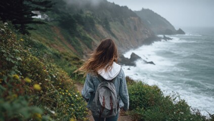 Woman with backpack walking on a coastal trail overlooking the ocean.