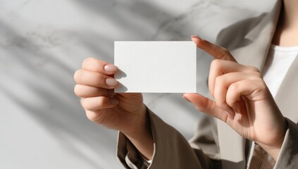 Womans hands holding a blank white business card with natural light and shadow overlay.