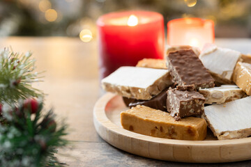Assorted traditional Christmas nougat on wooden plate and christmas tree background. Copy space