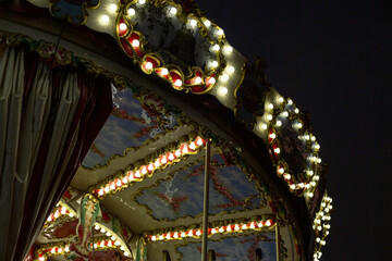 Close up of vintage carousel illuminated with bright lights, creating nostalgic, festive atmosphere. The colorful lights and details highlight the magic and fun of the fairground at night