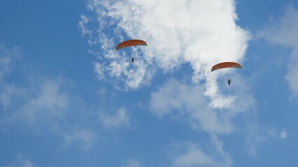 Two paramotors flying against vast, vibrant blue sky adorned with scattered white cumulus clouds. Each motorized paraglider unit, consisting of pilot operating engine propeller system, suspended - Powered by Adobe