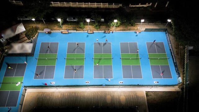 Aerial view of multiple pickleball courts with players in action, top down perspective of sport game, people playing recreational match under lights