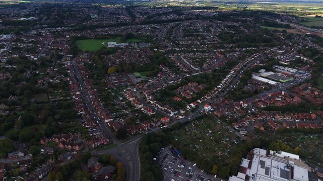 Aerial drone pans left over Fareham town village in Hampshire, England, capturing roads, cars, fields, and autumn trees glowing warmly in golden sunset light across the scenic countryside.