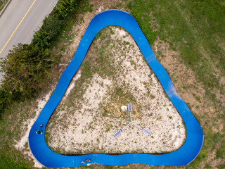 Aerial view of blue pump track with two kids riding scooters, top down perspective of outdoor...