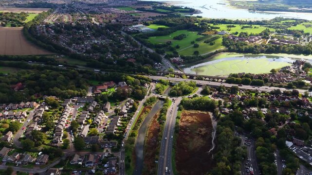 Aerial drone pans right over Fareham roundabout with river and water, capturing fields, roads, cars, and autumn nature glowing warmly in golden sunset light across the scenic English countryside.