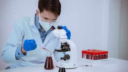 Serious Asian scientist researching blood in test tube. Man in white medical gown examining blood test tube in laboratory for DNA test.