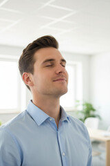 Man in light blue shirt is standing in bright office environment with his eyes closed, appearing calm and relaxed. setting suggests focus on mental health and workplace wellness solutions
