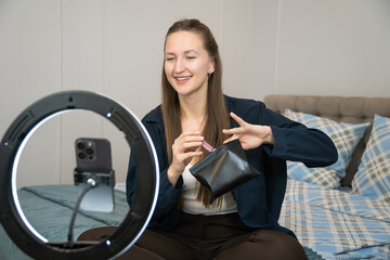 Influencer recording a makeup tutorial for social media channels, showcasing various cosmetics products while seated on a bed at home, engaging with followers and sharing beauty tips