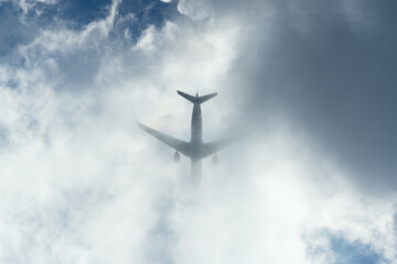 Silhouette of an airplane disappearing into dramatic clouds, view from below.