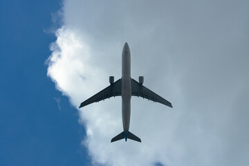 Underside view of a commercial airplane flying against a blue sky and white clouds.