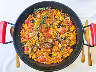 Top view of hot cast iron skillet with vegetarian paella with artichokes on white tablecloth